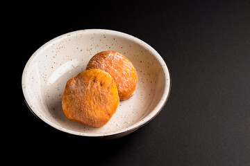 Two buttermilk dinner buns served in a white bowl over black background.