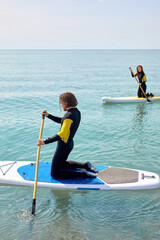 Paddle board sportsman standing paddling away on stand up paddleboarding at sea. Strong athlete male is standing on sup surfboard, watersport leisure activity.female in the background