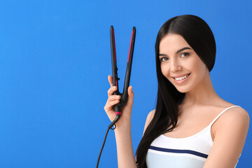 Beautiful young woman with flattening iron on color background