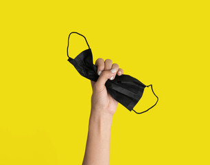 A hand holds face mask isolated on yellow background. Face covering. Virus protection. Medical and...