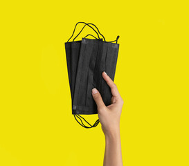 A hand holds face mask isolated on yellow background. Face covering. Virus protection. Medical and...