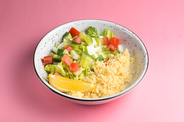 Bulgur with vegetables in a plate over pastel pink background. Delicious healthy dish in a bowl
