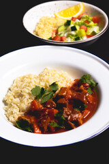 Chicken gravy with rice served in a white plate over black background.