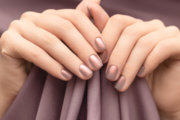 Female hands with beige nail design. Glitter beige nail polish manicure. Woman hands hold brown fabric background.