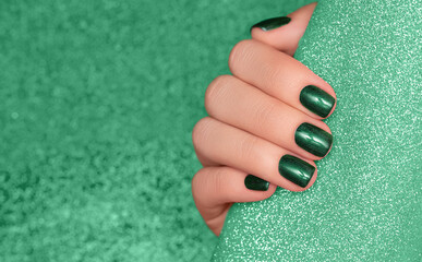 Female hand with green nail design. Glitter green nail polish manicure. Woman hand on glitter green fabric background - obrazy, fototapety, plakaty