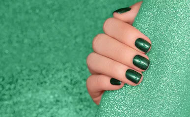Keuken spatwand met foto Female hand with green nail design. Glitter green nail polish manicure. Woman hand on glitter green fabric background © devmarya