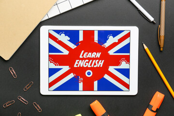 Fototapeta premium Tablet computer and stationery on dark background. Concept of learning English