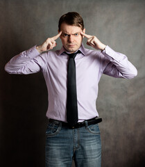 Portrait of pensive young man in pink shirt and dark tie, against dark background.