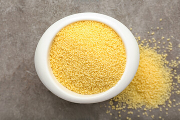 Bowl with raw couscous on grunge background, closeup