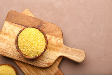 Bowl with raw couscous and board on color background