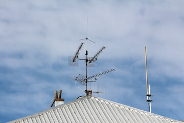 Various multiple TV and radio antennas in different shapes mounted on single strong metal pole next...