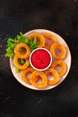Calamari rings. Squids with lettuce and tomato sauce, shot from above on a black background
