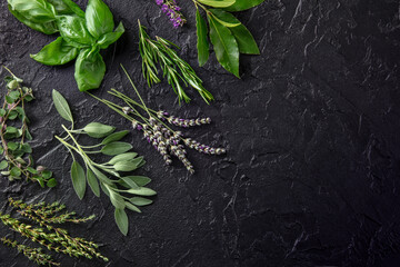 Fresh garden herbs, overhead flat lay shot on a black background with copy space. Bunches of rosemary, thyme, lavender and various other aromatic plants