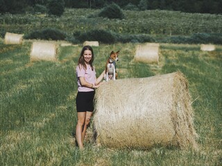 Naklejka na ściany i meble young woman with her Basenji dog on a field with haystacks
