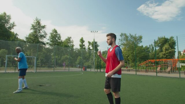 Soccer referee giving final whistle, notifying end of game match. Team of diverse multiethnic players in sportswear rejoicing win, giving high five on football pitch at daybreak