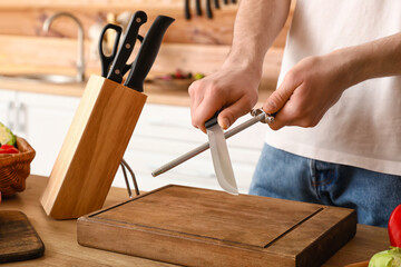 Man sharpening knife in kitchen, closeup