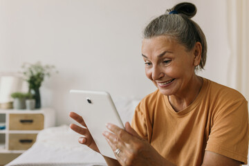 Smiling mature female talking to family on video call using tablet. Learn how to use modern device. Technology, communication, keep connection on distance concept. Copy space