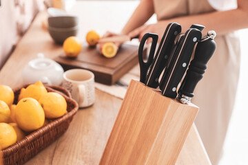 Stand with knives on table of woman cutting lemon in kitchen, closeup