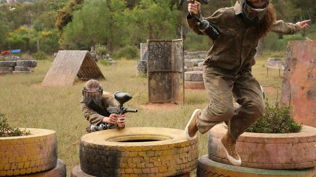 Excited male and female paintball players in protective uniform aiming and shooting with guns