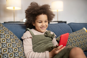 Smiling little girl with smartphone on sofa