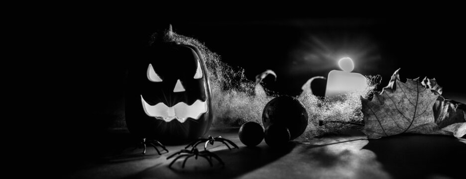 Black and white photo halloween pumpkins smile and scrary eyes for party night. Close up view of scary Halloween pumpkin with eyes glowing inside and candle at black background