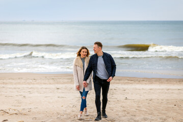Attractive young couple walking along the shore of a sandy beach, on a spring romantic holiday, outdoors.