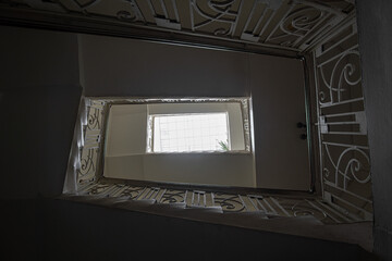 Dark staircase of an old multi-storey residential building of the 19th century with decorative railings and a window in the roof. Bottom-up view.