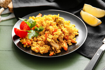 Fototapeta na wymiar Plate with tasty pilaf on color wooden background