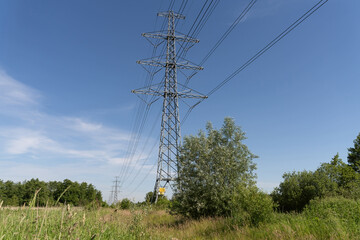 High-voltage electrical insulator electric line against the blue sky. In a natural landscape with grass and trees