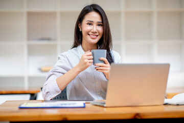 Portrait of asian Young beautiful lady drinking coffe and look to the working on laptop computer sitting in coffee shop, business report Financial and Accounting concept.