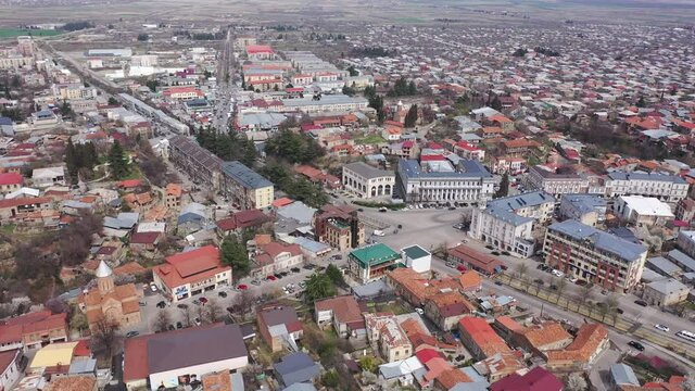 Scenic view from drone of central area of Telavi city overlooking large avenue with modern buildings surrounded by old small houses on spring day, Georgia