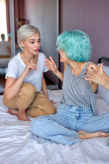 Obraz premium Two female friends or lesbians sitting on bed, arguing with each other. Friendship, quarrel, female disagreement, copy space. Angry friends or roommates sit quarelling, screaming, try to make up