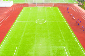 Football field with artificial turf and red running tracks, aerial view.