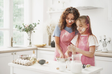 Mother and daughter having fun while cooking dough in kitchen