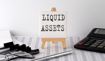 text LIQUID ASSETS on easel with office tools and paper.Top view. Business concept