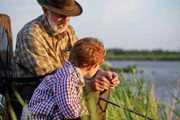 Grandfather mentoring grandson to fish at young age, side view, in nature, countryside. child boy...
