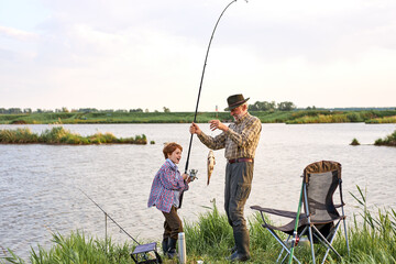 Man family fishing. cheerful Boy with grandfather catch the fish, fly fishing outdoor over river background. Old and young. Family time, hobby, happy childhood concept. copy space