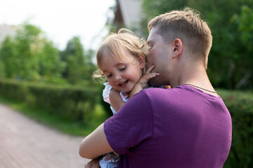 Young father kissing his little pretty daughter outdoors in summer day