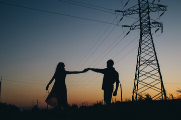 Fototapeta premium Couple dancing on the background of the sunset. Only the shadows and silhouettes of a man and a woman are visible. Dancers in the field. Next to a romantic pair of power lines. Romance and passion