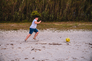 Niño en la playa jugando al futbol con un balón amarillo en la playa © Mac Estudio