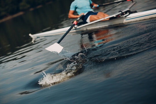 Sportsman single scull man rower rowing at competition boat regatta. Close up paddle splash water