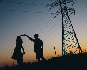 Couple dancing on the background of the sunset. Only the shadows and silhouettes of a man and a woman are visible. Dancers in the field. Next to a romantic pair of power lines. Romance and passion
