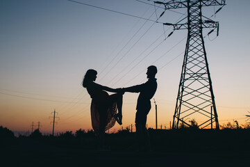 Couple dancing on the background of the sunset. Only the shadows and silhouettes of a man and a woman are visible. Dancers in the field. Next to a romantic pair of power lines. Romance and passion