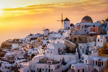 The windmills and whitewashed houses of Oia at Santorini island, Greece, during golden summer sunset time