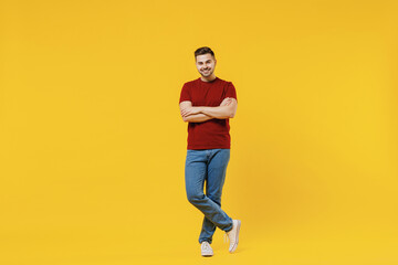Full length smiling caucasian happy young man 20s wear red t-shirt casual clothes holding hands crossed folded isolated on plain yellow color wall background studio portrait. People lifestyle concept.
