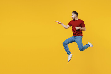 Fototapeta na wymiar Full length excited young man in red t-shirt casual clothes jump high point index finger aside workspace area isolated on plain yellow color wall background studio portrait People lifestyle concept