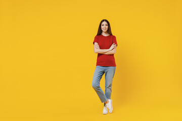 Full size body length excited smiling happy young brunette woman 20s wears basic red t-shirt stand hold hands crossed isolated on yellow background studio portrait. People emotions lifestyle concept.