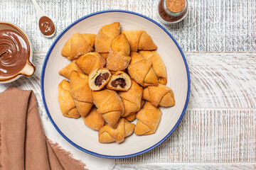 Homemade filled rolled pastries with chocolate. Made with butter and cream cheese doughs. White wooden surface.