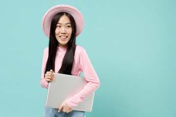 Charming smiling slender businesslike young brunette asian woman 20s wears pink clothes holding laptop pc computer under her hand look aside isolated on pastel blue color background studio portrait