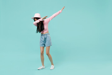 Full size body length young brunette asian woman 20s wears pink clothes doing dab hip hop dance hands move gesture youth sign hide cover face isolated on pastel blue color background studio portrait